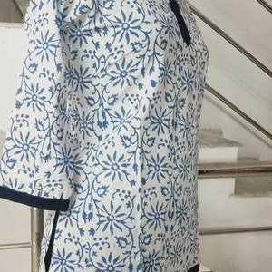 May include: A white and blue floral print tunic with a dark blue trim. The tunic has a mandarin collar and three-quarter sleeves.