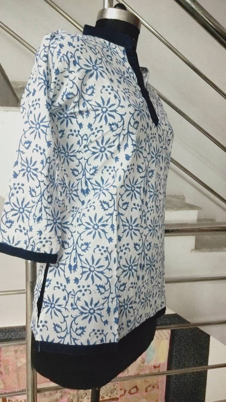 May include: A white and blue floral print tunic with a dark blue trim. The tunic has a mandarin collar and three-quarter sleeves.