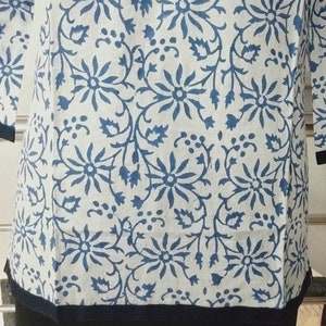 May include: A white cotton top with a blue floral print and a black trim around the bottom.