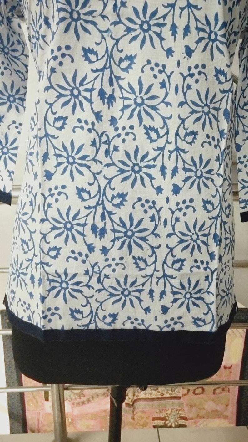 May include: A white cotton top with a blue floral print and a black trim around the bottom.