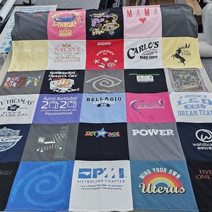 May include: A quilt made from a variety of t-shirts, featuring different designs and text. The quilt is made up of 16 squares, each with a different design. Some of the designs include a heart, a crown, a butterfly, a skull, a rainbow, and a star. The text on the quilt includes the words "Mama", "Mom", "St. Thomas", "April Birthday 2020", "Belllagio", "LSD", "Power", "SPI", "Mind Your Own Uterus", and "Five Kings, One Throne".