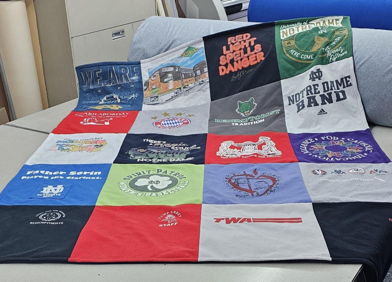 May include: A patchwork quilt made from various t-shirts. The quilt is made up of 16 squares, each with a different design. Some of the designs include the words "Red Light Spells Danger", "Notre Dame Band", and "Spirit Patrol".