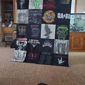 May include: A patchwork quilt made from various band t-shirts. The quilt features bands such as Avenged Sevenfold, Slipknot, and Metallica. The quilt is black and white with some red, green, and blue accents.