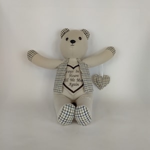 May include: A beige teddy bear with a brown heart on its chest that says "Always In Heart Till We Meet Again". The bear is wearing a plaid waistcoat and has a small plaid heart hanging from its arm.