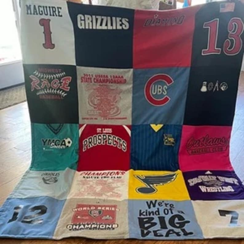 May include: A patchwork quilt made from various t-shirts. The quilt is made up of 16 squares, each with a different design. Some of the designs include sports team logos, school names, and other phrases. The quilt is a great way to commemorate a special event or to show your support for your favorite teams.