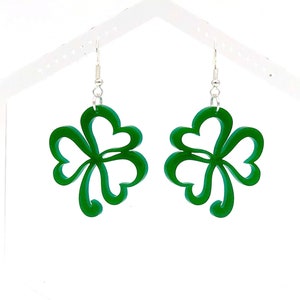 May include: A pair of green shamrock earrings with silver hooks. The shamrocks are made of a layered, cut-out design.