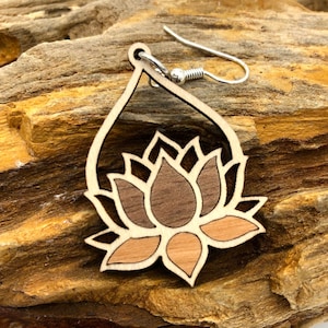 Könnte beinhalten: Ein Paar Holzohrringe mit einem Lotusblumen-Design. Die Ohrringe sind aus verschiedenen Holzschattierungen gefertigt, darunter Braun, Hellbraun und Naturholz. Die Ohrringe haben einen silbernen Haken.
