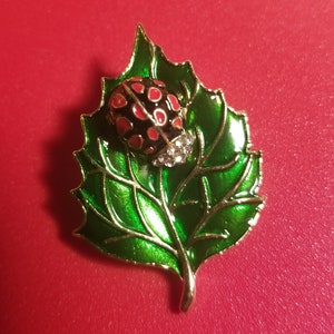 May include: A gold-tone brooch featuring a red and black ladybug on a green enamel leaf.