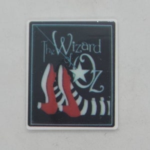 May include: A black and white image of ruby red slippers with a white star and the text "The Wizard of Oz" on a black background.