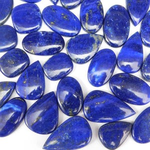 May include: A collection of polished lapis lazuli gemstones in various shapes, including oval, teardrop, and irregular forms. The deep blue stones have gold flecks and a glossy finish, ideal for jewelry making or collecting.