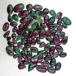 May include: A collection of green and red gemstone cabochons. The stones are various shapes and sizes, with a mix of green and red colors.