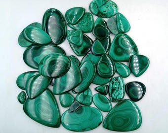 May include: A collection of polished malachite gemstones in various shapes, including ovals, teardrops, and freeform designs. The stones display a rich, swirling pattern of dark and light green hues, with a glossy finish.