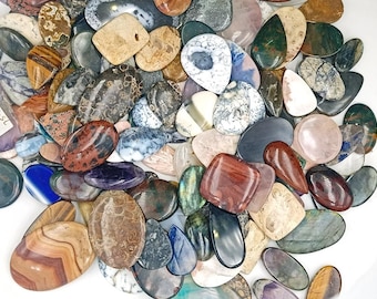 Peut inclure: Assortiment de cabochons en pierres précieuses naturelles polies de différentes formes, tailles et couleurs. Les cabochons sont disposés sur une surface blanche. Certaines des pierres comprennent l'agate, le jaspe et l'améthyste.