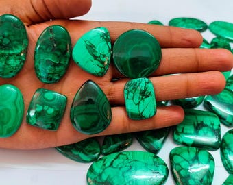 May include: A collection of polished malachite gemstones in various shapes, including ovals, circles, and teardrops. The stones display a vibrant green color with unique swirling patterns. Some stones are held in a hand, while others are scattered around.