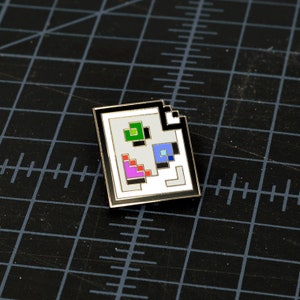 May include: A white enamel pin with a black border, depicting a stylized image of a QR code with colored squares. The pin is on a black grid background.