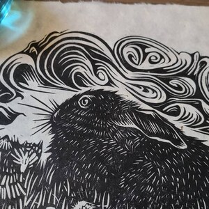 May include: Black and white linocut print of a rabbit with swirling clouds and a full moon in the background.