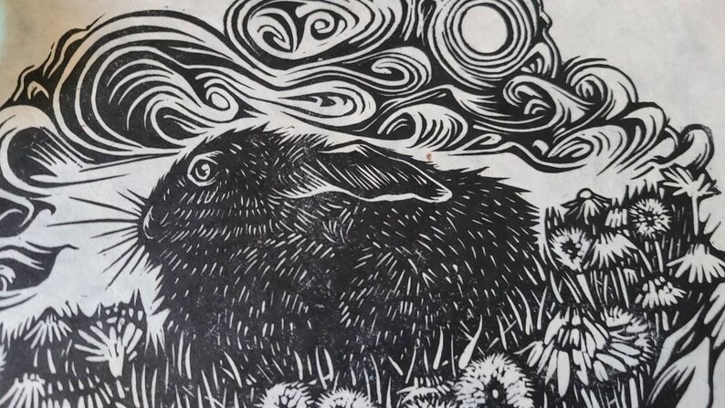 May include: Black and white woodcut print of a rabbit with a swirling cloud above it. The rabbit is surrounded by stylized flowers.