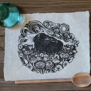 May include: Black and white linocut print of a rabbit in a field of flowers. The rabbit is looking to the right and the flowers are in bloom. The print is on a white background.