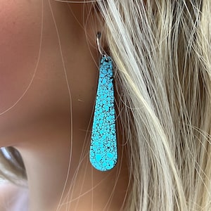 May include: A pair of turquoise dangle earrings with a speckled pattern. The earrings are made of metal and have a silver hook.
