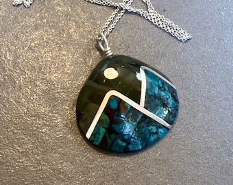 Puede incluir: Un collar de cadena de plata con un colgante hecho de turquesa y piedras negras. El colgante tiene forma de lágrima y tiene un diseño geométrico.