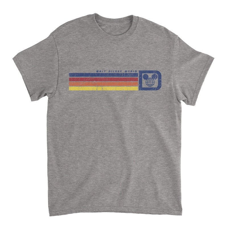 May include: A heather gray t-shirt featuring a retro design with the text "WALT DISNEY WORLD". The design includes horizontal stripes in red, orange, yellow, and a blue rectangle with the Mickey Mouse globe logo. The shirt has a crew neck and short sleeves.