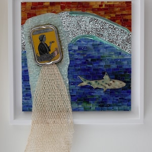 Puede incluir: Una obra de arte en mosaico que representa una ola rompiendo sobre una pequeña lata amarilla con la imagen de una mujer y el texto "Sardines garanties très à l'huile" y "La Douarmente" en ella. Una red de pesca blanca cuelga de la lata y un tiburón de mosaico azul y verde nada debajo de la ola.