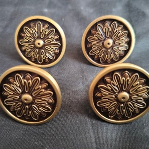 Puede incluir: Cuatro pomos de armario de metal dorado con un diseño floral decorativo. Los pomos tienen un diseño circular en relieve con un círculo central y líneas radiales.