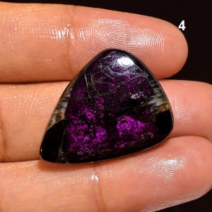May include: A purple and black gemstone cabochon with a triangular shape. The gemstone has a unique pattern of black and white veins.