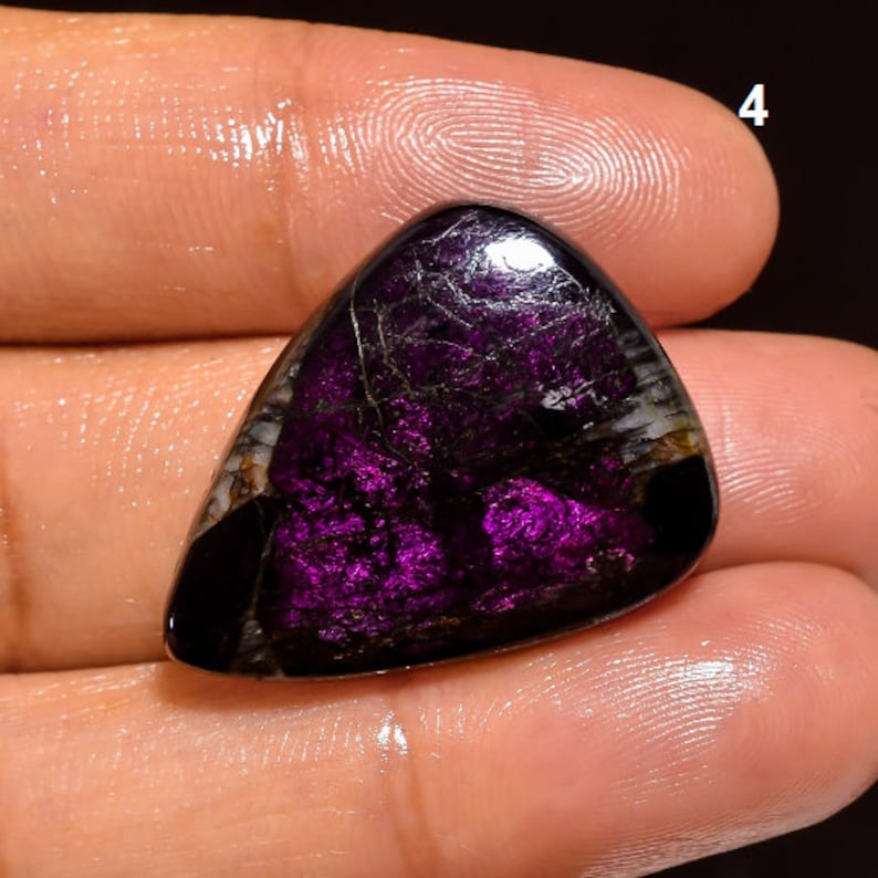 May include: A purple and black gemstone cabochon with a triangular shape. The gemstone has a unique pattern of black and white veins.