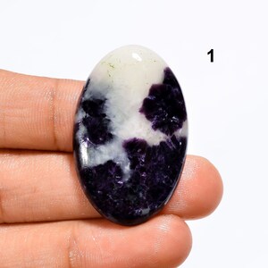 May include: Oval shaped cabochon gemstone with a white and purple pattern. The stone has a smooth, polished surface.