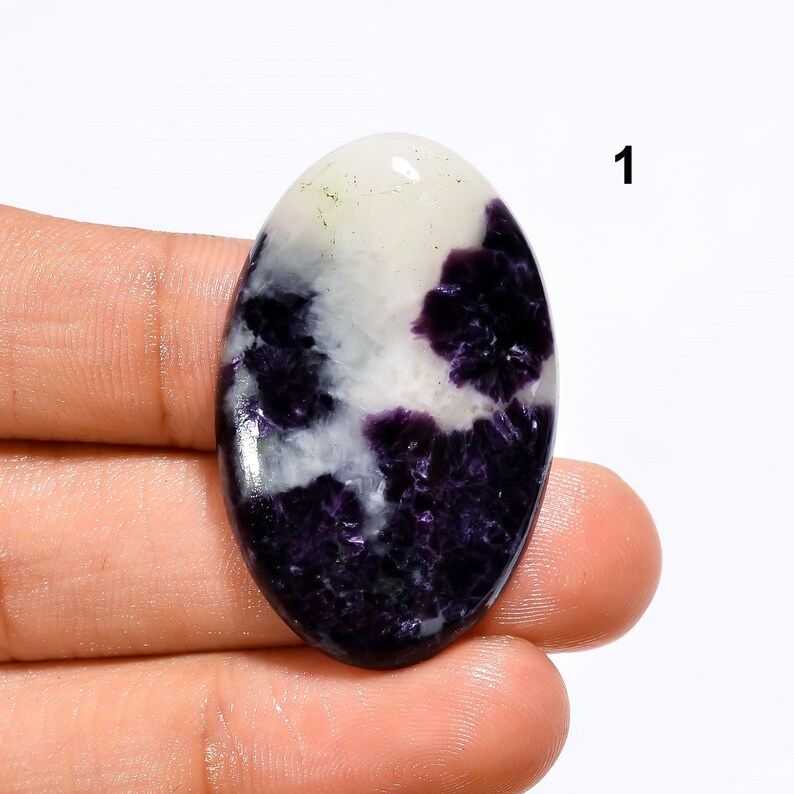 May include: Oval shaped cabochon gemstone with a white and purple pattern. The stone has a smooth, polished surface.
