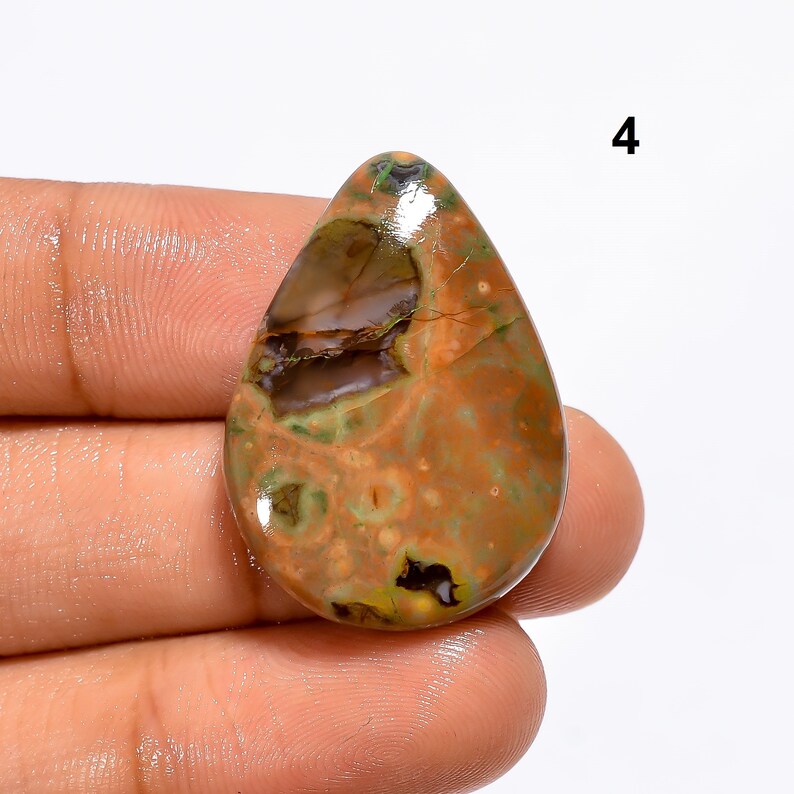 May include: A teardrop-shaped, green, brown, and orange gemstone cabochon with a mottled pattern. The stone is polished and has a glossy finish.