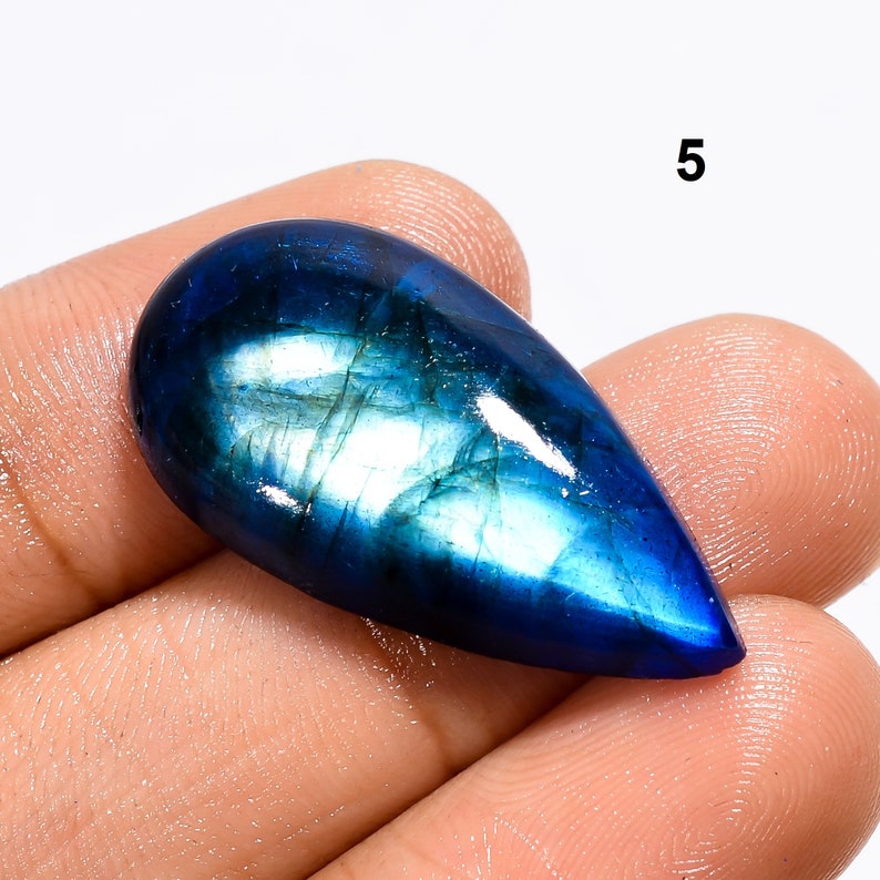 May include: A teardrop-shaped blue labradorite gemstone with iridescent flashes of color. The gemstone is approximately 2 inches long and 1 inch wide.