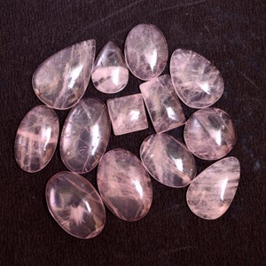 Puede incluir: Una colección de 11 cabujones de cuarzo rosa de diferentes formas y tamaños. Las piedras son translúcidas y tienen un color rosa claro.