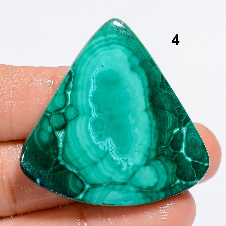 May include: A green malachite cabochon with a triangular shape and a swirling pattern. The stone has a smooth, polished surface.