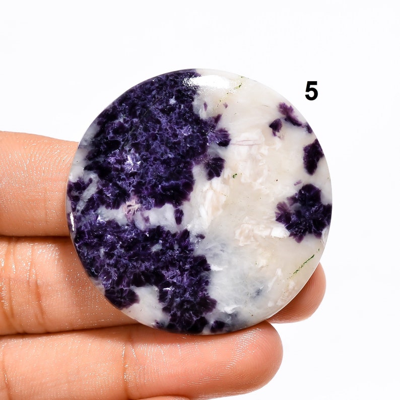 May include: Round, polished cabochon of purple and white opal. The stone has a swirling pattern of purple and white.