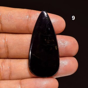 May include: A black teardrop-shaped gemstone with gold flecks. The gemstone is approximately 2 inches long.