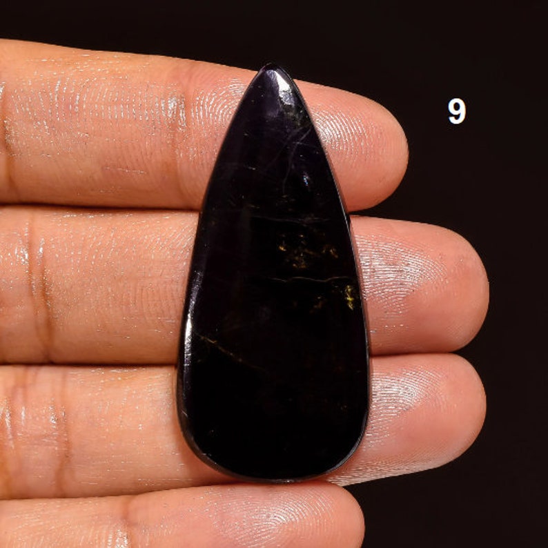 May include: A black teardrop-shaped gemstone with gold flecks. The gemstone is approximately 2 inches long.