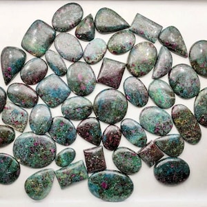 May include: A collection of green and pink ruby zoisite cabochons, a type of gemstone, in various shapes and sizes.