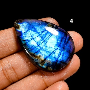 Puede incluir: Una piedra preciosa de labradorita en forma de lágrima con una superficie pulida que muestra una iridiscencia azul y púrpura vibrante y fracturas internas. El número 4 aparece en la esquina superior derecha sobre un fondo negro.