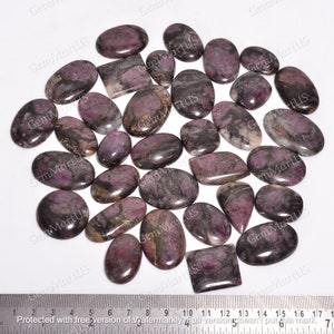 May include: A collection of 25 purple and black gemstone cabochons. The cabochons are oval and rectangular shaped and have a polished finish.