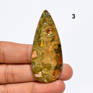 May include: A teardrop-shaped green, brown, and orange gemstone cabochon with a mottled pattern. The stone is approximately 3 cm long and 2 cm wide.