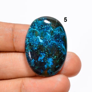 Pu&ograve; includere: Pietra preziosa ovale a cabochon con un motivo blu, verde e nero. La pietra ha una superficie liscia e lucida.