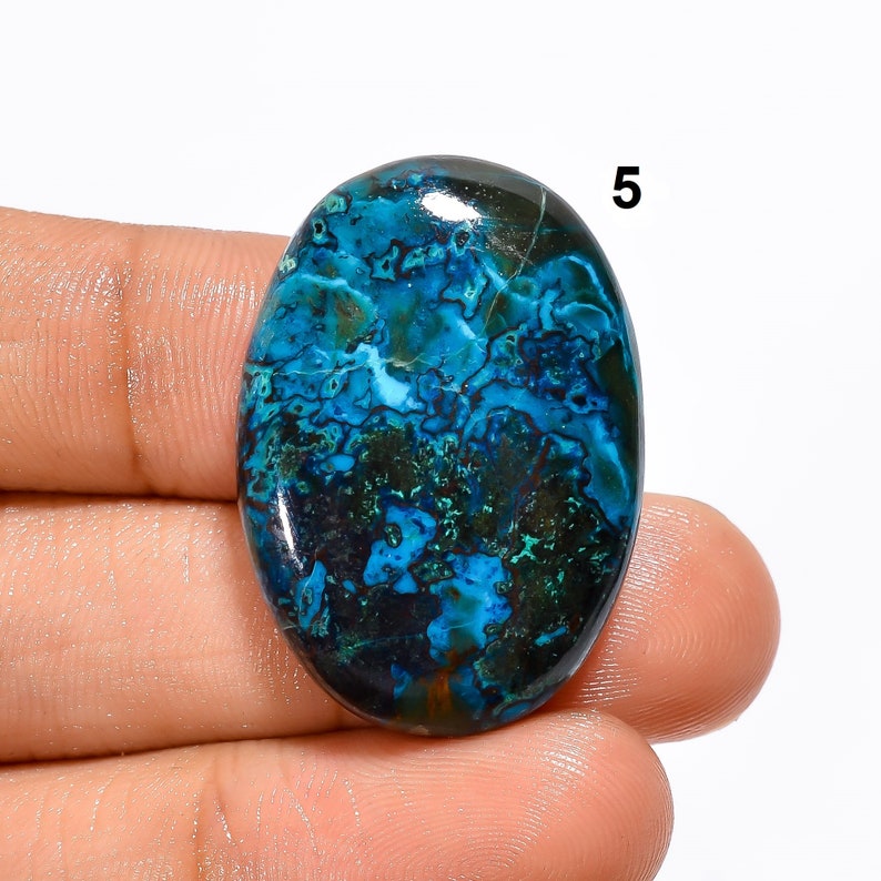 Pu&ograve; includere: Pietra preziosa ovale a cabochon con un motivo blu, verde e nero. La pietra ha una superficie liscia e lucida.