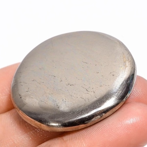 Pode incluir: Uma pedra de pirita redonda e lisa de cor prateada. A pedra tem um brilho metálico ligeiramente e é polida a um acabamento liso.