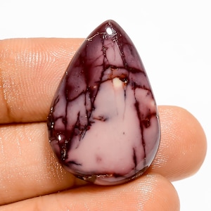 May include: A polished, teardrop-shaped gemstone with a mix of colors. The stone features a base of pale pink with dark burgundy veining and accents. The gem is held in a hand, showcasing its smooth, glossy surface.