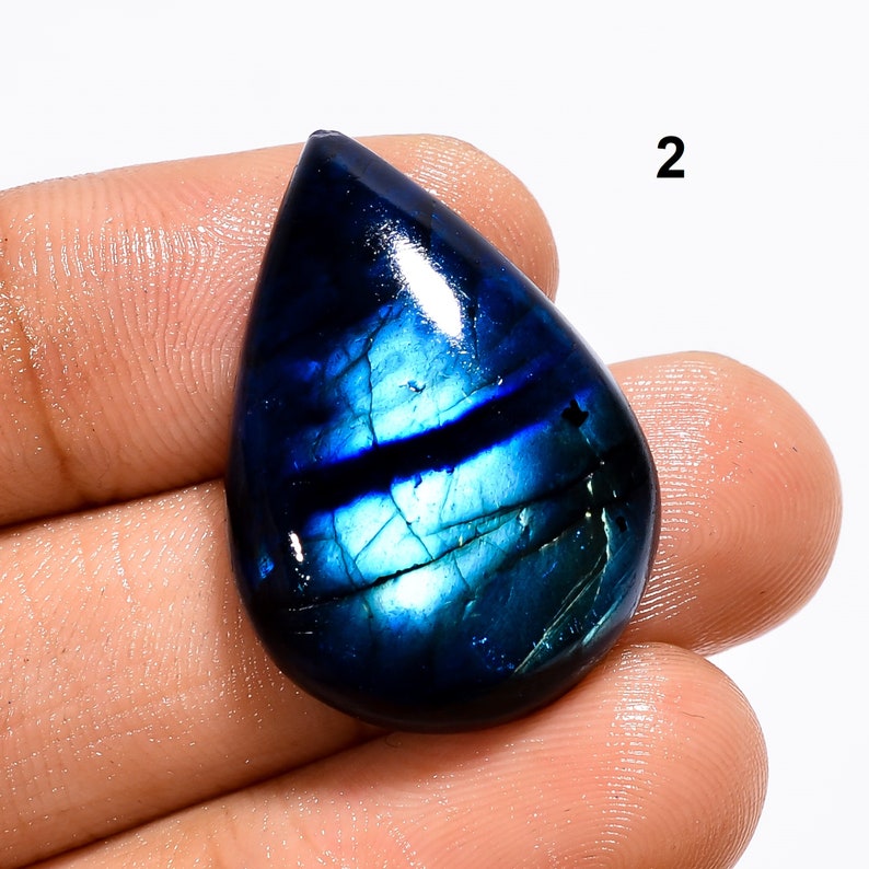May include: A teardrop-shaped blue labradorite gemstone cabochon with iridescent flashes of green and blue.