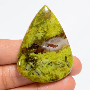 May include: A green, yellow, and brown gemstone cabochon with a teardrop shape. The stone has a unique pattern of swirls and veins.