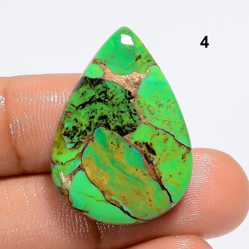 May include: A green and gold turquoise cabochon with a teardrop shape. The stone has a natural, organic pattern with copper inclusions.