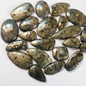 Könnte beinhalten: Eine Sammlung von 18 Pyrit-Cabochons in verschiedenen Formen und Größen. Die Steine sind eine Mischung aus Silber- und Goldtönen mit einem gesprenkelten Muster.